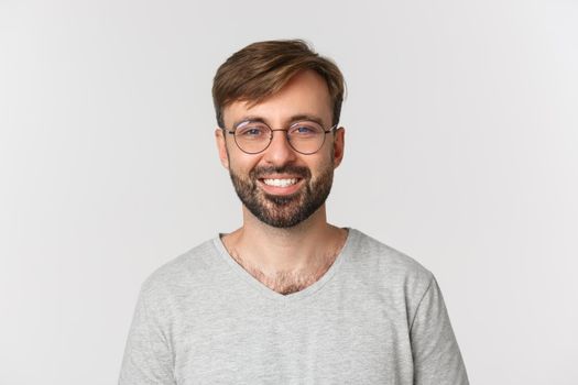 Close-up of handsome modern guy in glasses, smiling and looking at camera, standing over white background.