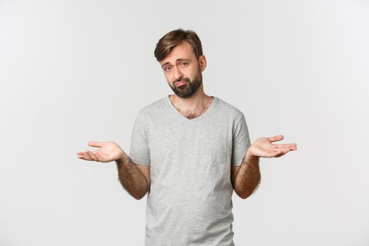 Portrait of indecisive sad guy with beard, shrugging with hands spread sideways, standing clueless over white background.