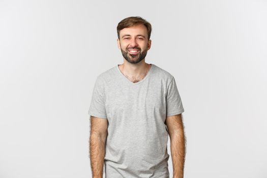 Handsome caucasian guy with beard, standing in grey basic t-shirt and smiling happy.