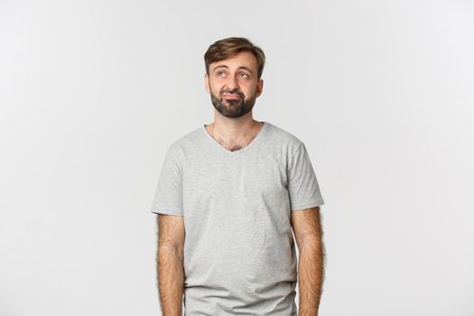 Portrait of gloomy guy feeling like a loser, looking at upper left corner reluctant, standing over white background.