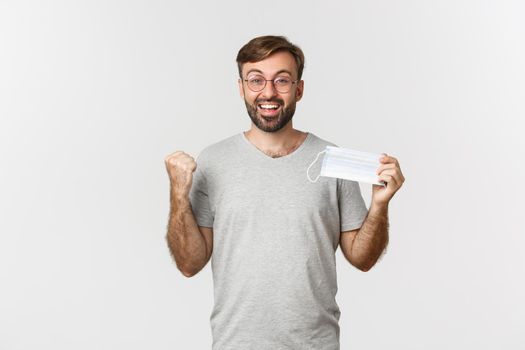 Concept of pandemic, coronavirus and social-distancing. Image of handsome smiling guy in glasses, clench fist excited and recommending to wear medical mask.