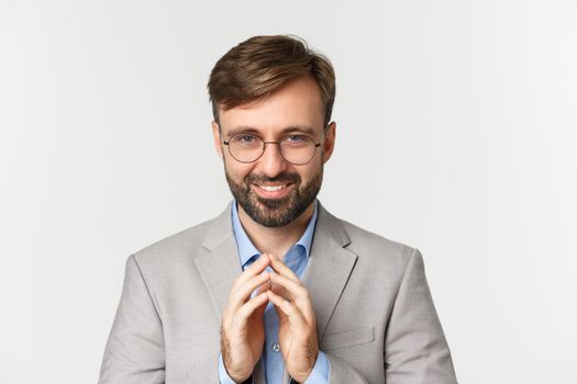 Close-up of bearded businessman in glasses and suit, scheming something, smiling devious and having perfect plan, standing over white background.