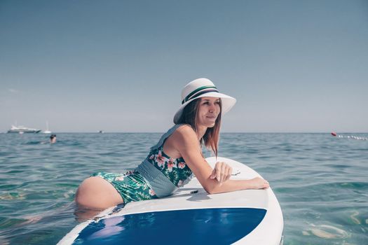 Happy young woman in swimsuits doing yoga on sup board in calm sea, early morning. Balanced pose - concept of healthy life and natural balance between body and mental development