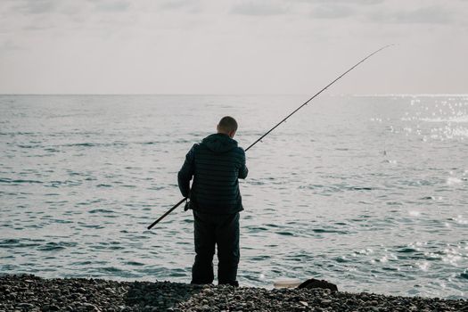 Man hobby fishing on sea tightens a fishing line reel of fish summer. Calm surface sea. Close-up of a fisherman hands twist reel with fishing line on a rod. Fishing in the blue sea outdoors
