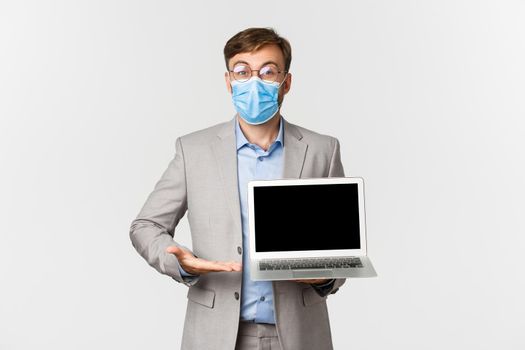 Concept of work, covid-19 and social distancing. Portrait of impressed boss in medical mask, showing something amazing on laptop screen, demonstrating presentation, white background.