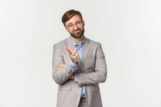 Portrait of doubtful businessman with beard, wearing glasses and suit, grimacing and looking skeptical, standing indecisive over white background.