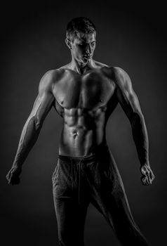 Sexy muscular man posing with naked torso in studio and looking behind on black background. Black and white