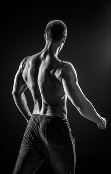 Stunning muscular man fitness model torso showing muscles back and shoulders on black background. Black and white