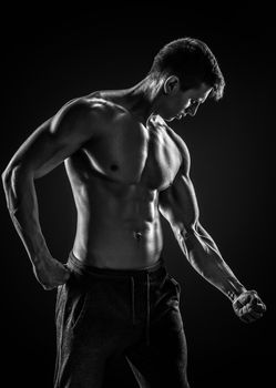 Strong bodybuilder man posing with perfect abs, houlders,biceps, triceps and chest on black background. Black and white