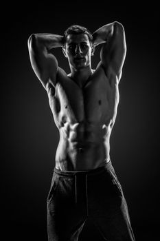 Sexy shirtless bodybuilder posing and looking at camera on black background. Extreme strength, muscles and fitness.. Black and white