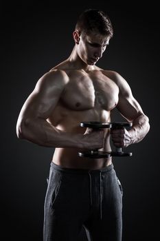 Mighty fitness man showing his gread body with dumbbells in hand on black background.