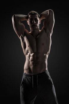 Sexy shirtless bodybuilder posing and looking at camera on black background. Extreme strength, muscles and fitness.