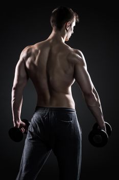 Muscular fitness man showing his gread body with dumbbells in hand on black background, rear view.