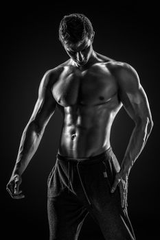 Sporty and healthy man posing and showing his perfect boddy on black background. Black and white