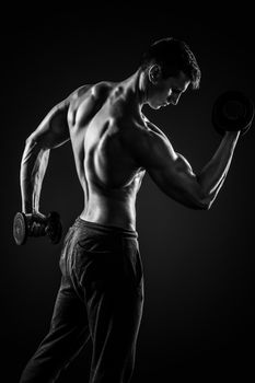 Fitness man working out doing exercises with dumbbells at biceps on black background, rear view. Black and white