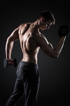 Fitness man working out doing exercises with dumbbells at biceps on black background, rear view
