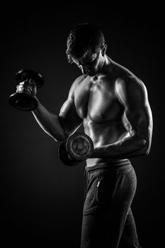 Athletic man showing muscular body and doing exercises with dumbbells on black background.. Black and white