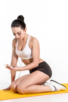 Brunette with fit body on yoga mat. girl with phone and headphones. Healthy lifestyle and sports concept.