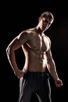 Strong bodybuilder man posing with perfect abs, houlders,biceps, triceps and chest on black background.