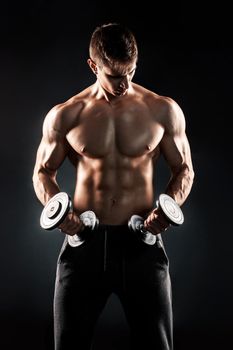 Mighty fitness man showing his gread body with dumbbells in hand on black background..