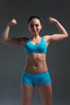 Muscular young woman athlete standing looking at the camera. Raise your hands up. It shows strength