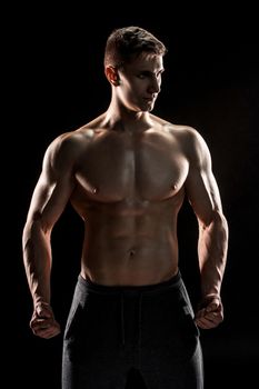 Sexy muscular man posing with naked torso in studio and looking behind on black background