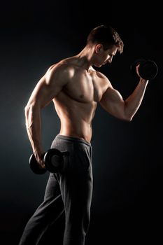 Athletic man showing muscular body and doing exercises with dumbbells on black background..