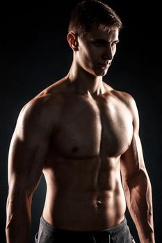 Mighty fitness man showing his gread body with dumbbells in hand on black background. Close up