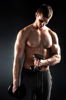 Mighty fitness man showing his gread body with dumbbells in hand on black background..