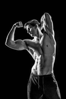 Strong bodybuilder man posing with perfect abs, houlders,biceps, triceps and chest on black background. Black and white