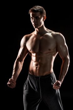 Sexy muscular man posing with naked torso in studio and looking behind on black background.