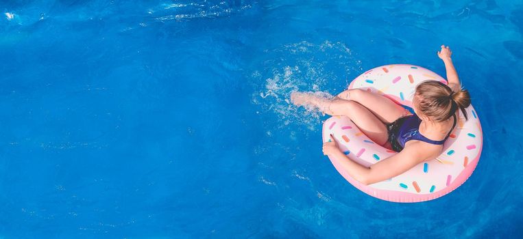 Banner Summer warm vacation. A girl sits on a rubber ring in the form of a donut in a blue pool. Time to relax on an air mattress. Fun in the water for a family holiday. Seaside resort. Copy space