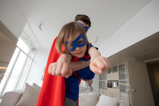 Father holding son flying in superhero costume at home