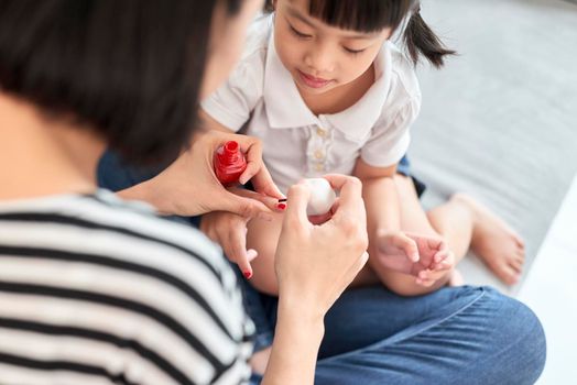 Beautiful young mother is painting the nail varnish to her cute little daughter