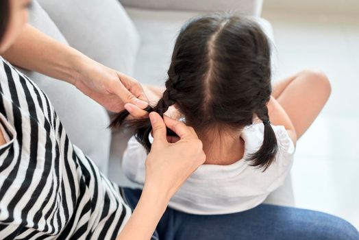 mother braiding hair of her daughter