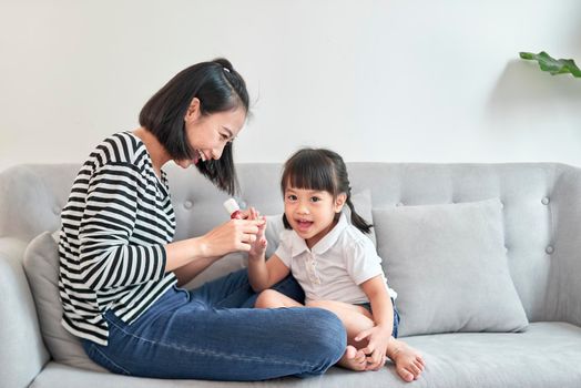 Beautiful young mother is painting the nail varnish to her cute little daughter