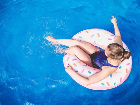 Summer warm vacation. The girl sits on a rubber ring in the form of a donut in a blue pool. Time to relax on an air mattress. Having fun in the water for a family vacation. Sea resort. Copy space.