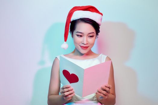 beautiful young woman holding a valentine postcard with a pink heart on light background