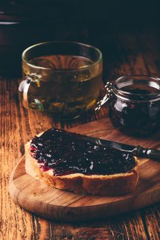 Toast with berry jam on cutting board and cup of green tea