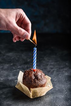 Hand lighting candle with a match on birthday chocolate muffin