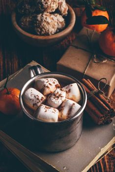Rustic metal mug of hot chocolate with marshmallows. Tangerines, cinnamon sticks bunch and gingerbread.