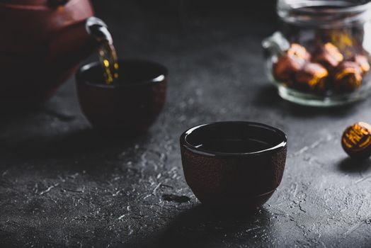 Pouring ready red tea from iron kettle into tea bowl