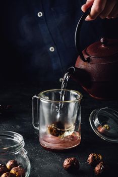 Steeping red tea in glass mug. Pouring boiled water from iron kettle.