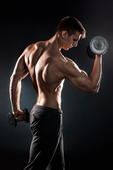 Young handsome man with naked torso and dumbbells in hand on black background.