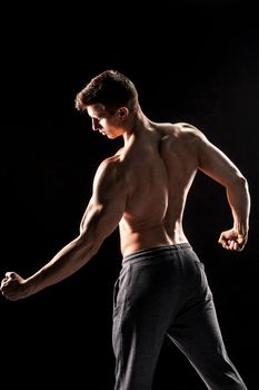 Strong bodybuilder man posing with perfect abs, houlders,biceps, triceps and chest on black background.