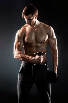 Mighty fitness man showing his gread body with dumbbells in hand on black background..
