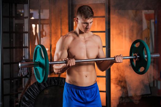 young man doing exercises with barbell in gym. Orange smoke on background