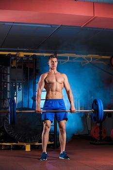 young man doing exercises with barbell in gym. blue smoke in the background