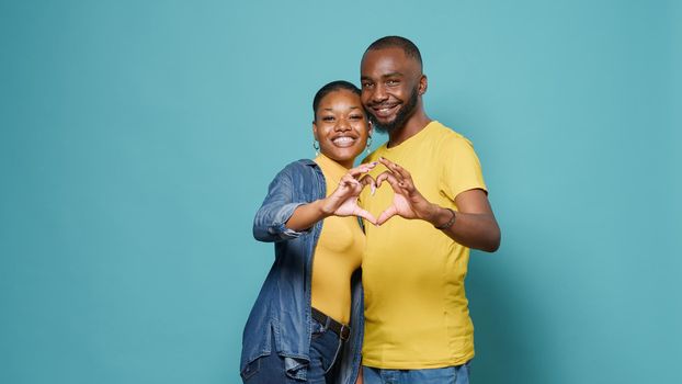 People in love advertising heart shape sign with hands in front of camera. Affectionate couple doing romantic and intimate symbol, showing gesture of affection, romance and feelings.