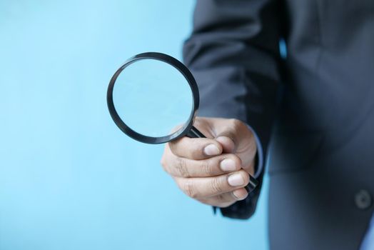 hand holding magnifying glass against blue background .